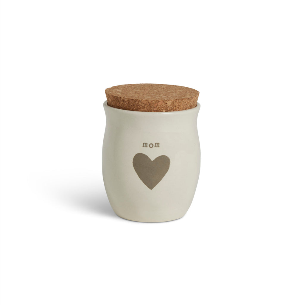 A cream ceramic candle with a gray heart and the word "mom". The candle has a cork lid.