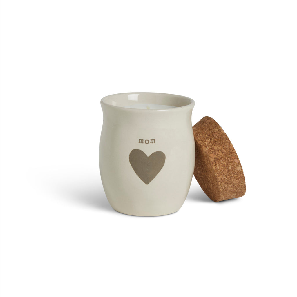 A cream ceramic candle with a gray heart and the word "mom". The candle has a cork lid, displayed with the lid off and leaning on the side.