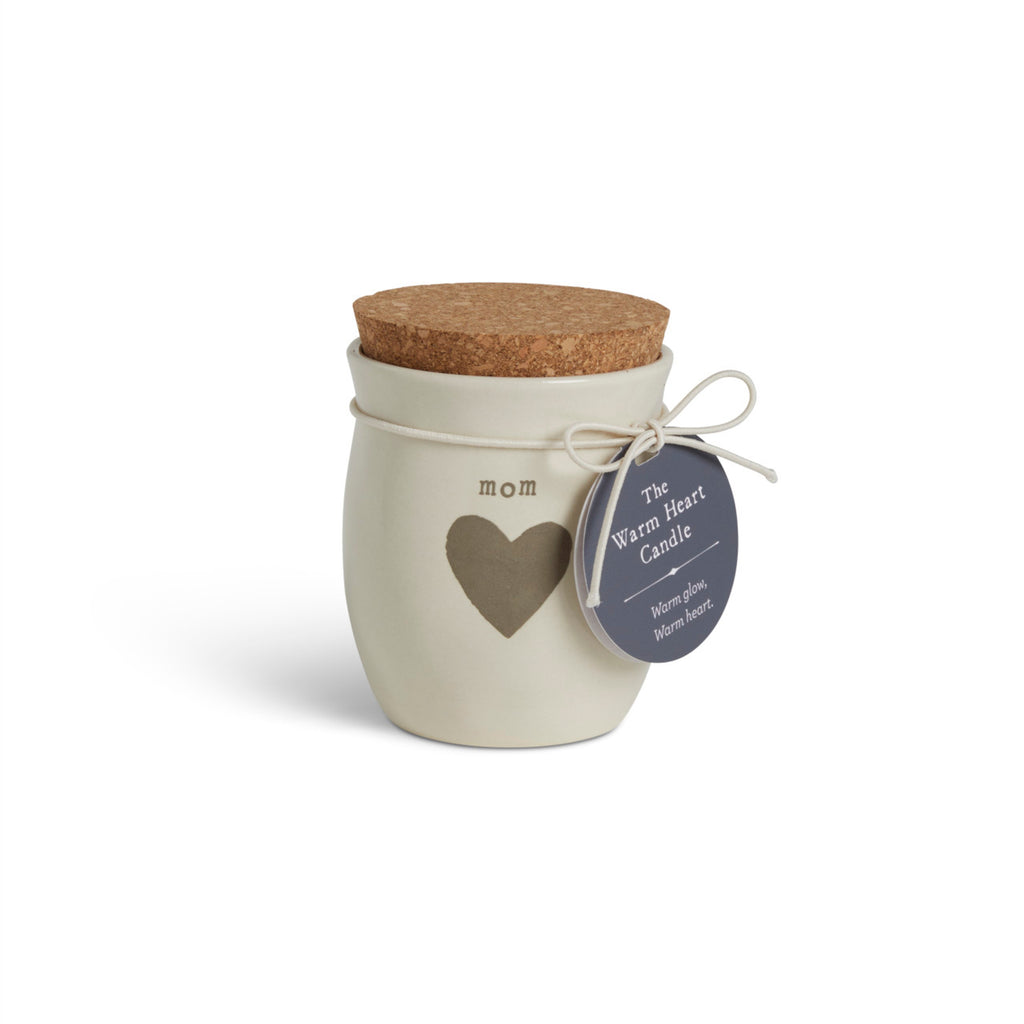 A cream ceramic candle with a gray heart and the word "mom". The candle has a cork lid, displayed with a product tag attached.