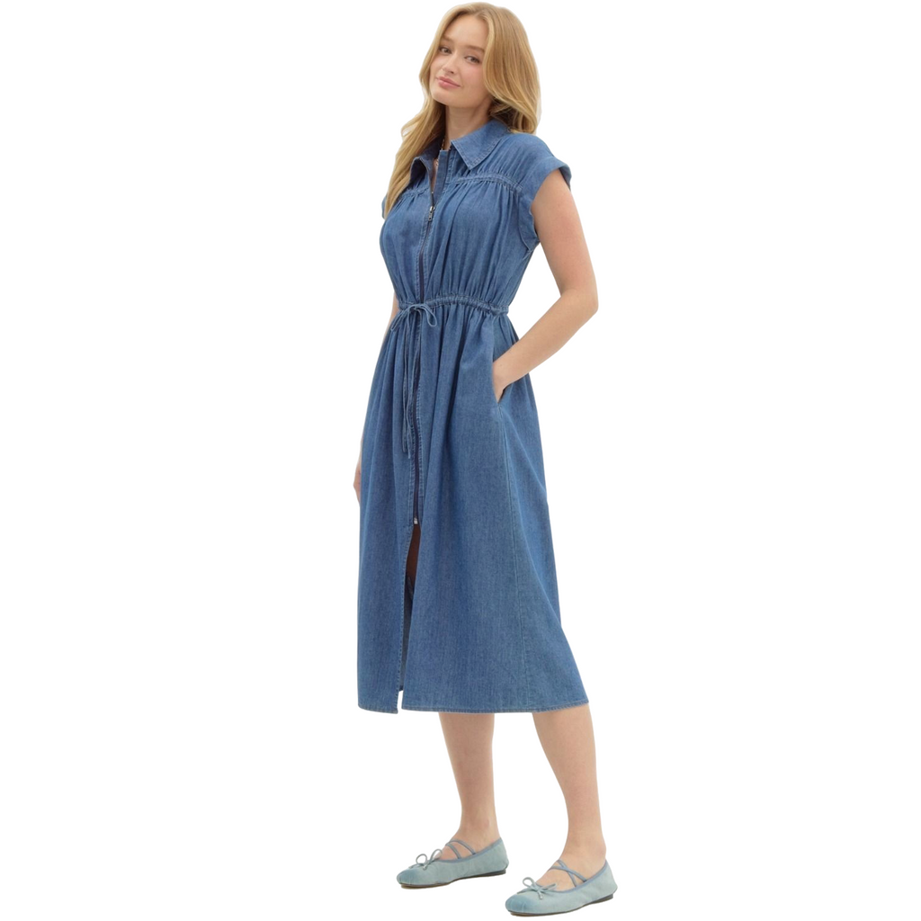 A woman is wearing a knee-length, short-sleeved denim dress with a collar, a full-length zipper down the front, and a drawstring waist.