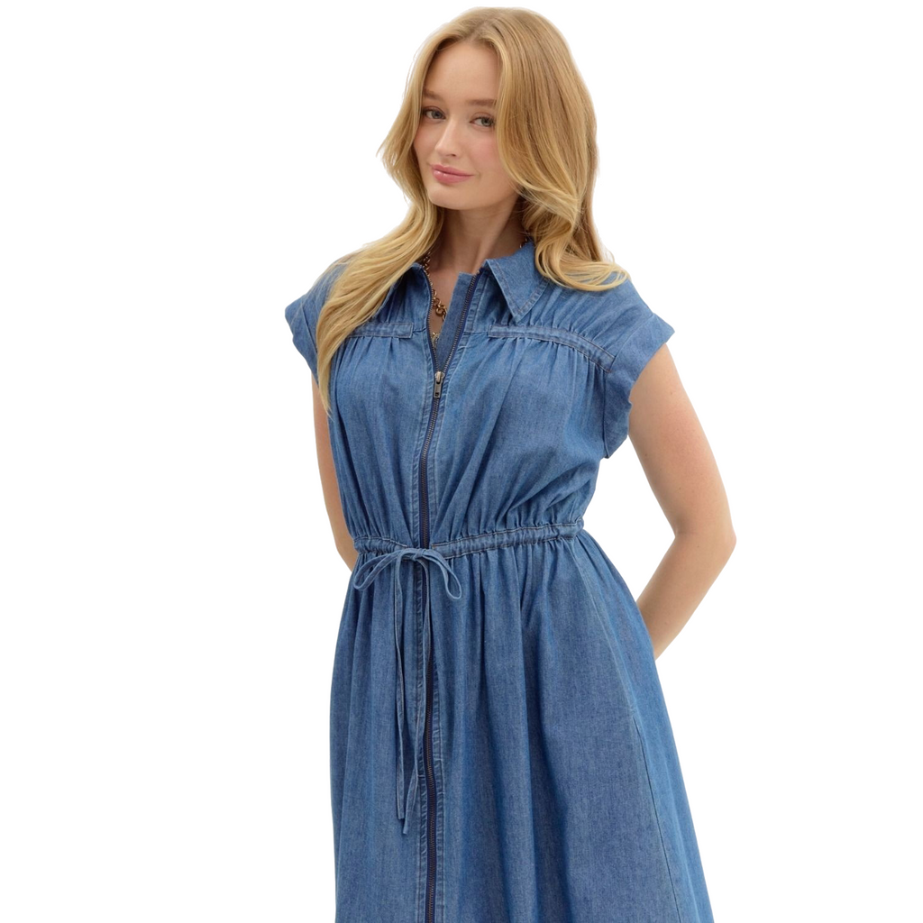 A woman is wearing a knee-length, short-sleeved denim dress with a collar, a full-length zipper down the front, and a drawstring waist.