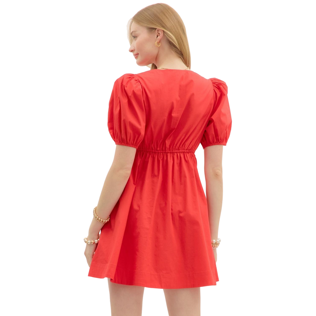 A woman wearing a bright red mini dress. The dress features a V-neckline, short puff sleeves, and a pleated A-line skirt.