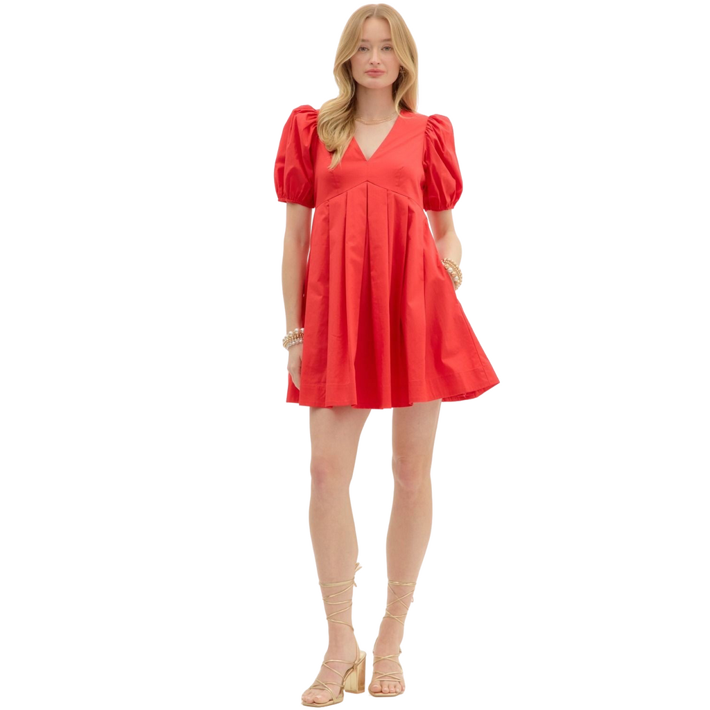 A woman wearing a bright red mini dress. The dress features a V-neckline, short puff sleeves, and a pleated A-line skirt.