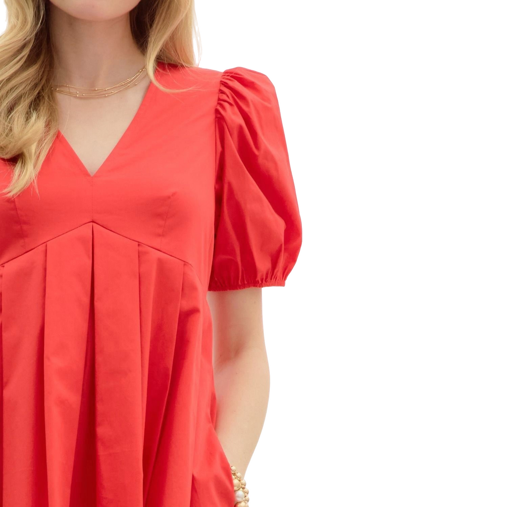 A woman wearing a bright red mini dress. The dress features a V-neckline, short puff sleeves, and a pleated A-line skirt.