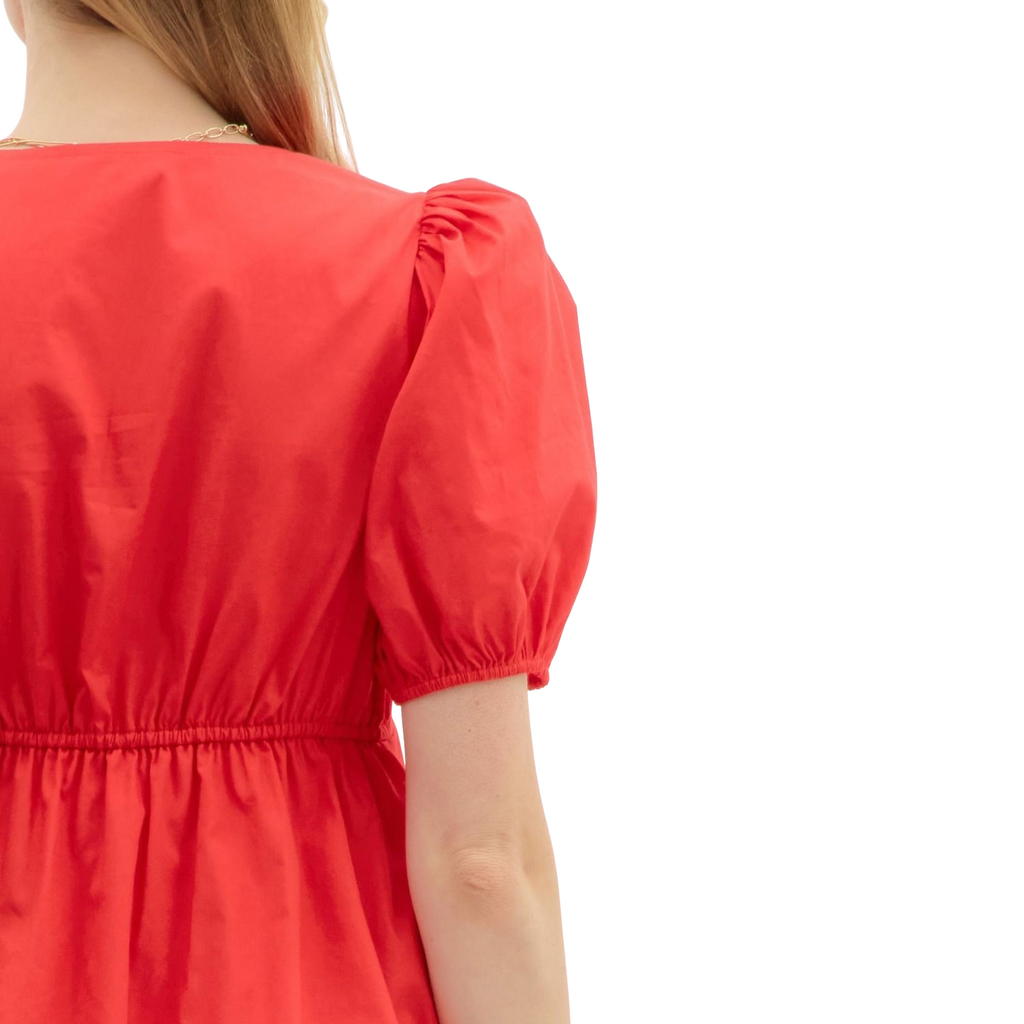 A woman wearing a bright red mini dress. The dress features a V-neckline, short puff sleeves, and a pleated A-line skirt.